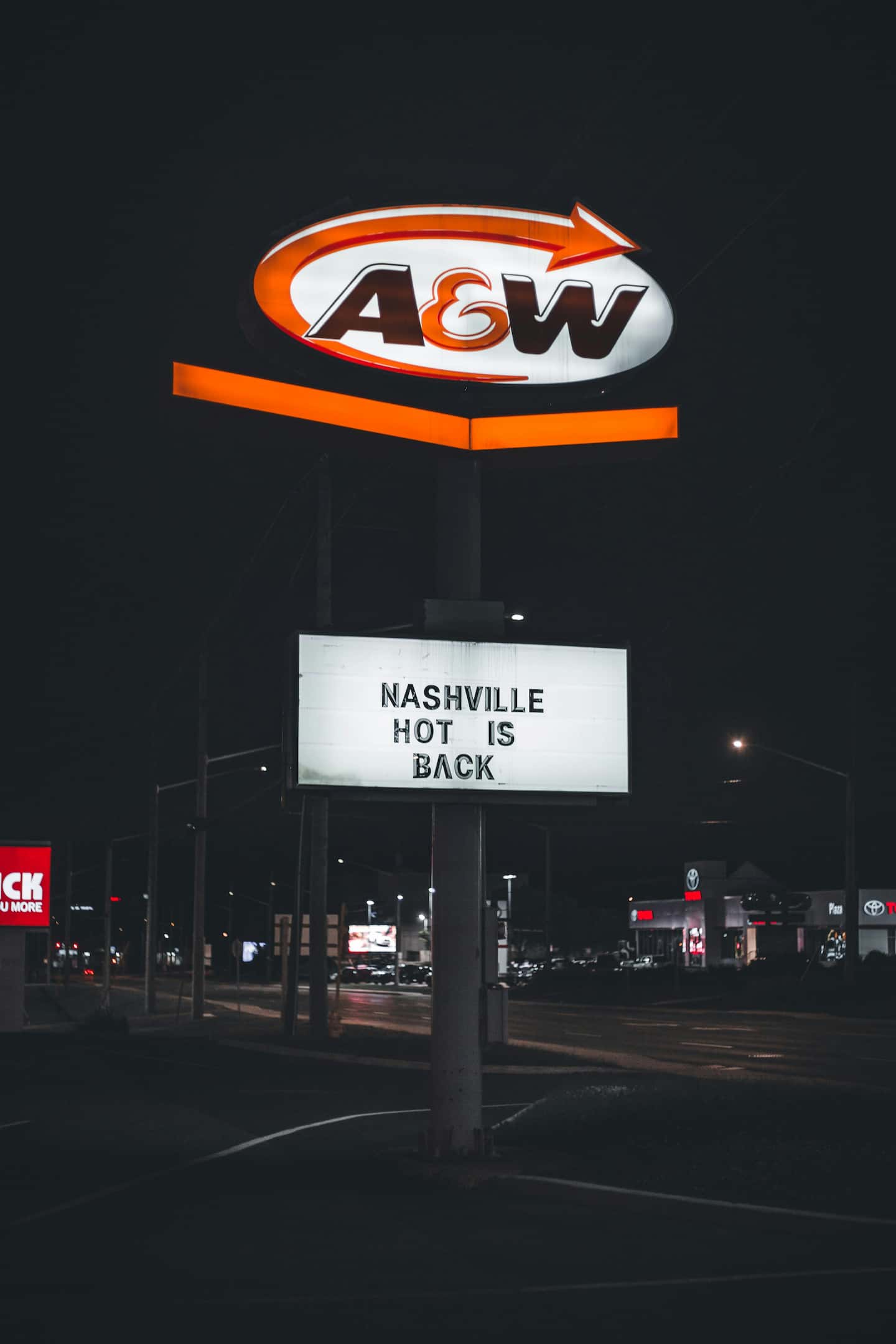 Fast-food pylon sign at night showing an illuminated A&W logo above a message board with text "NASHVILLE HOT IS BACK".