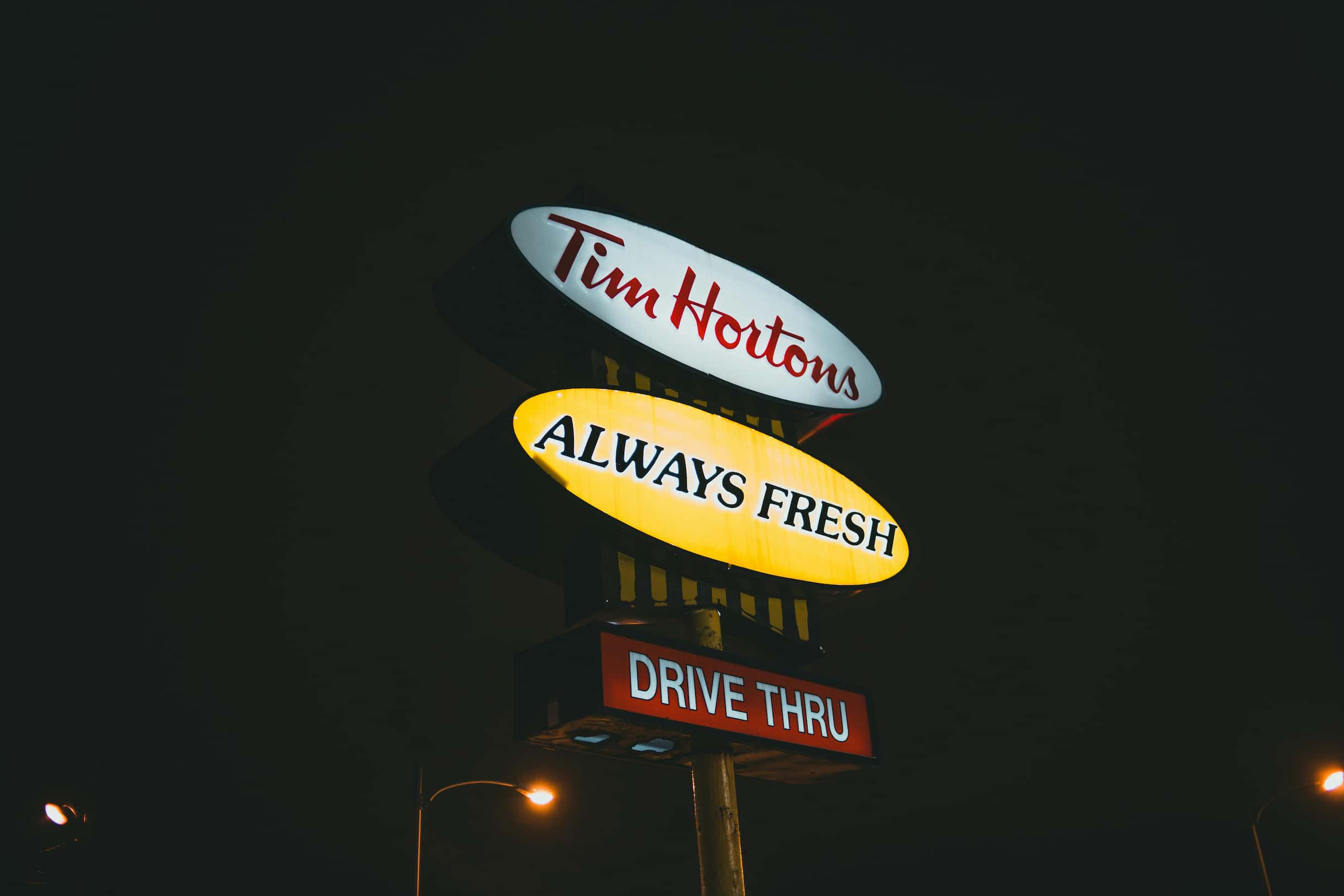 illuminated-tim-hortons-fast-food-pylon-sign-at-night.jpg Alt Text: Multi-brand fast-food pylon sign at night featuring illuminated Tim Hortons logo, "ALWAYS FRESH", and "DRIVE THRU" text panels.