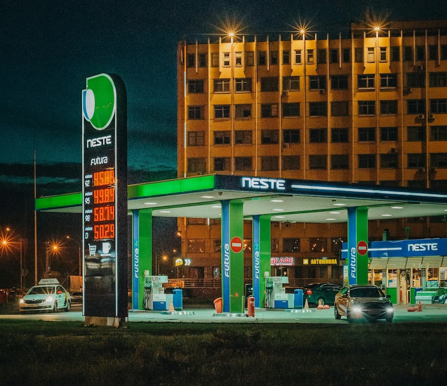 Canopy and tall totem sign of a Neste petrol station under night lighting with urban background.